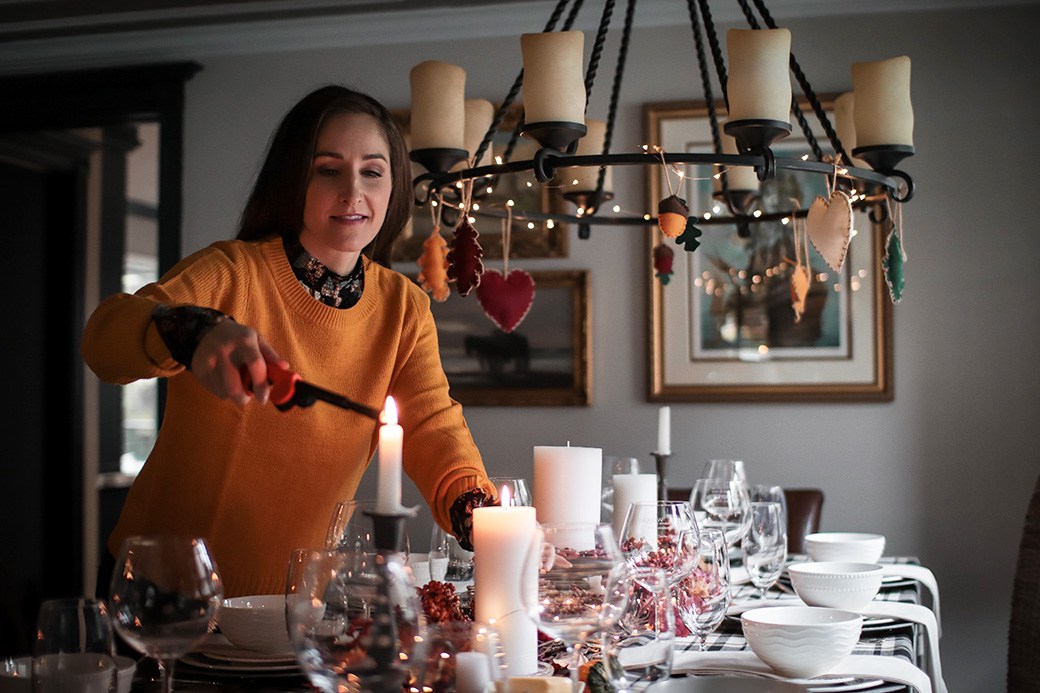Woman lighting candle on dinner table with Thanksgiving decor
