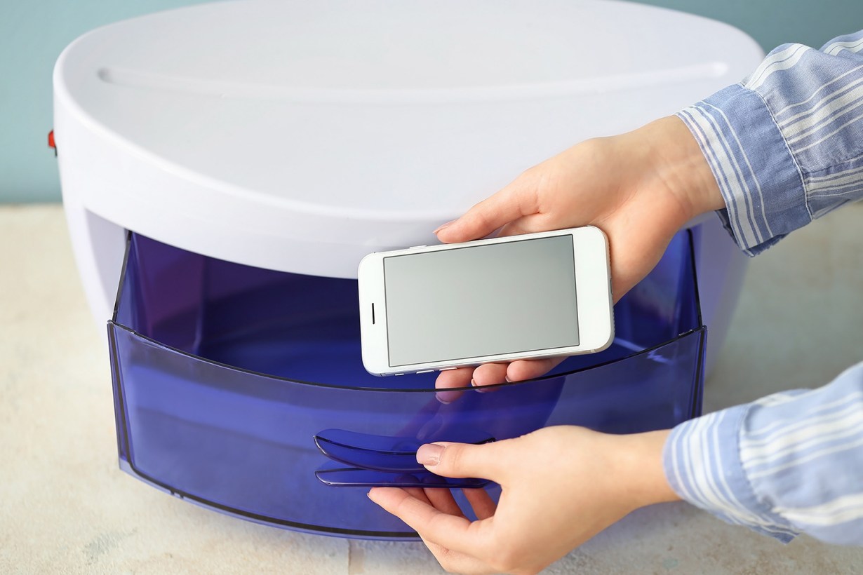a hand putting a smartphone inside a uv sanitizer