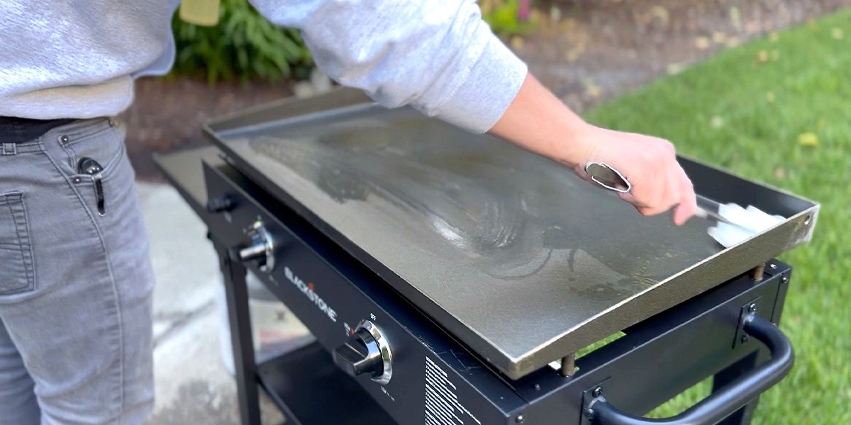 Person cleaning flat-top grill on lawn